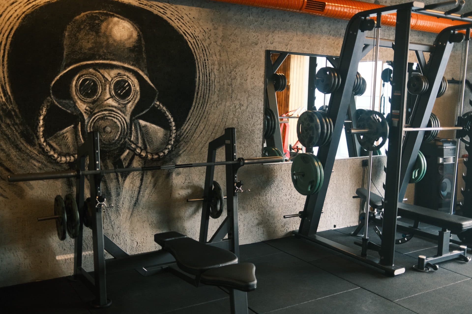 Dairesel çerçeveli karakalem gaz maskeli asker muralı önünde halter yüklü squat ve bench rafı